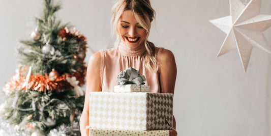 Woman holding presents beside a christmas tree