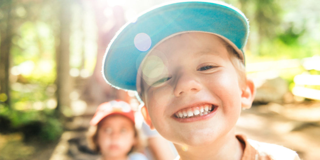 a child smiling wearing a blue hat surrounded by greenery
