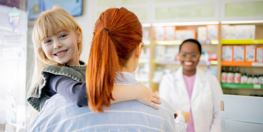 a mother with red hair holding her child while talking with a pharmacist