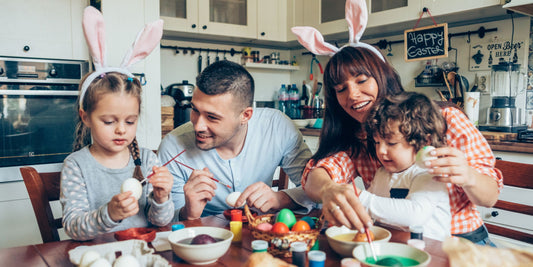 A joyful family, wearing bunny ears, gathers around a table to decorate Easter eggs in their cozy kitchen