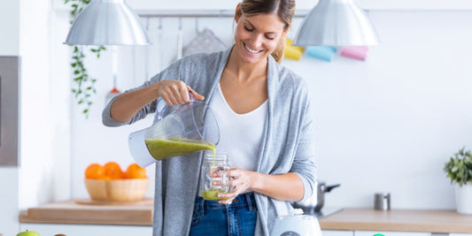A person pouring a green smoothie into a glass jar in a bright, modern kitchen