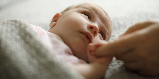 a baby laying down holding a person's finger