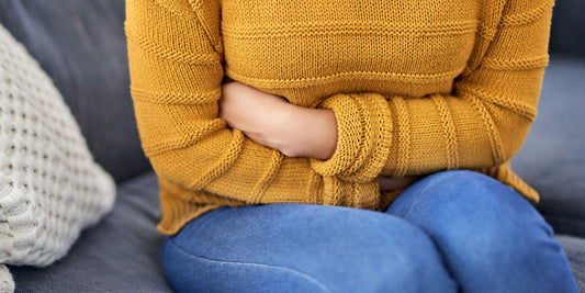 woman wearing a yellow sweater and sitting on a couch holding her arms around her stomach