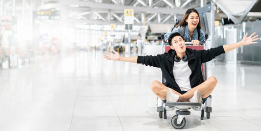 Happy woman pushing happy man on a trolley in an airport