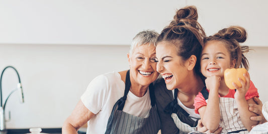a grandmother, mother, and child holding each other and laughing in the kitchen
