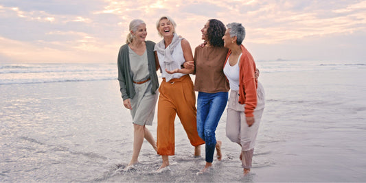 a group of mature women walking together on a beach and laughing in shallow water